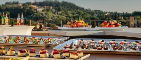 Ein Dachterrassen-Essbereich mit verschiedenen Desserts und Snacks auf Tabletts, mit Blick auf eine malerische Hügellandschaft.