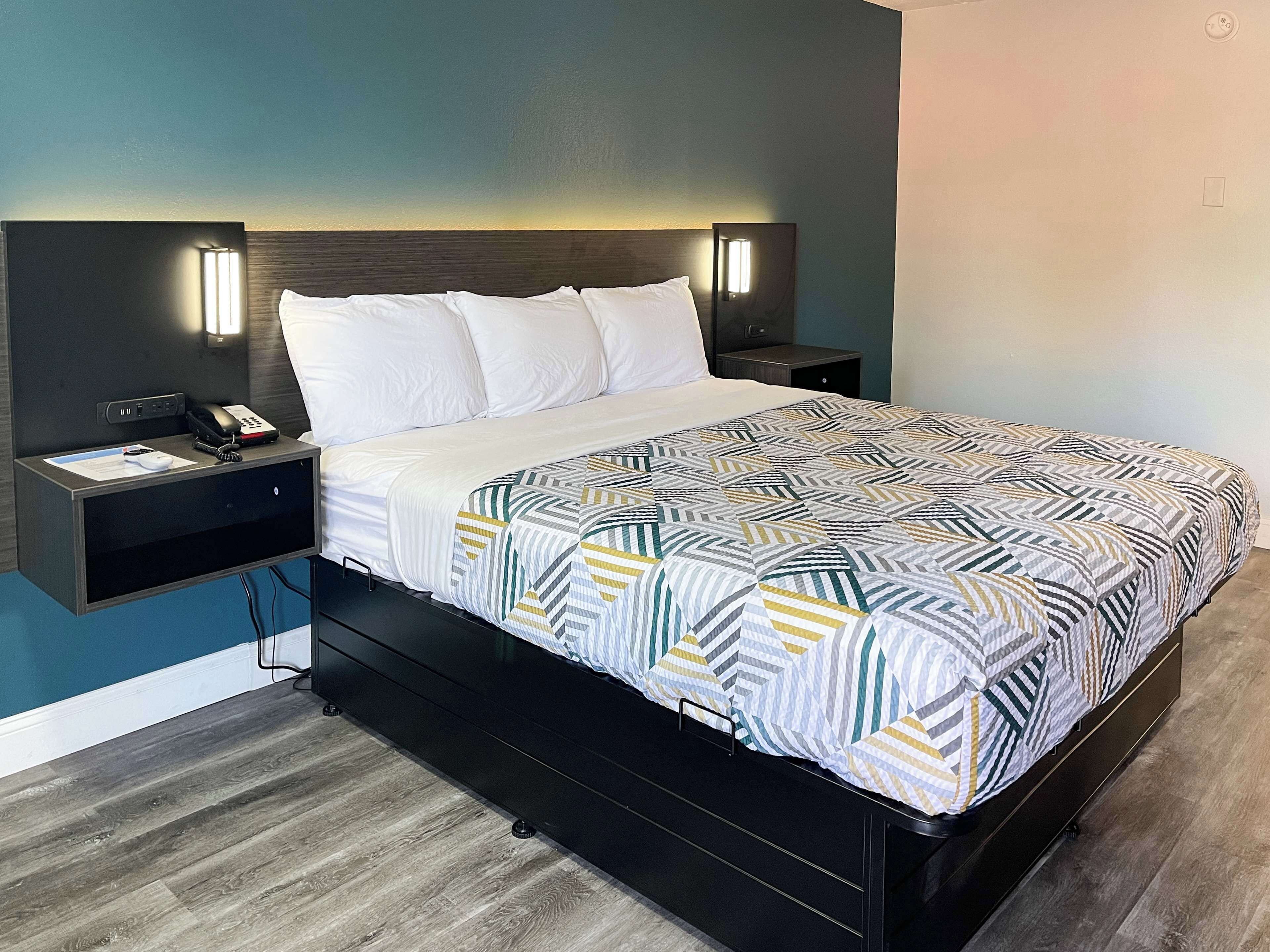 A modern hotel room with a bed, bedside tables, and a headboard with integrated lighting.