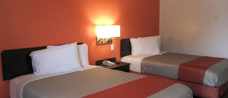 Habitación de hotel con dos camas, cada una con cubrecama rojo y blanco, una mesita de noche con teléfono y una lámpara fijada a la pared.
