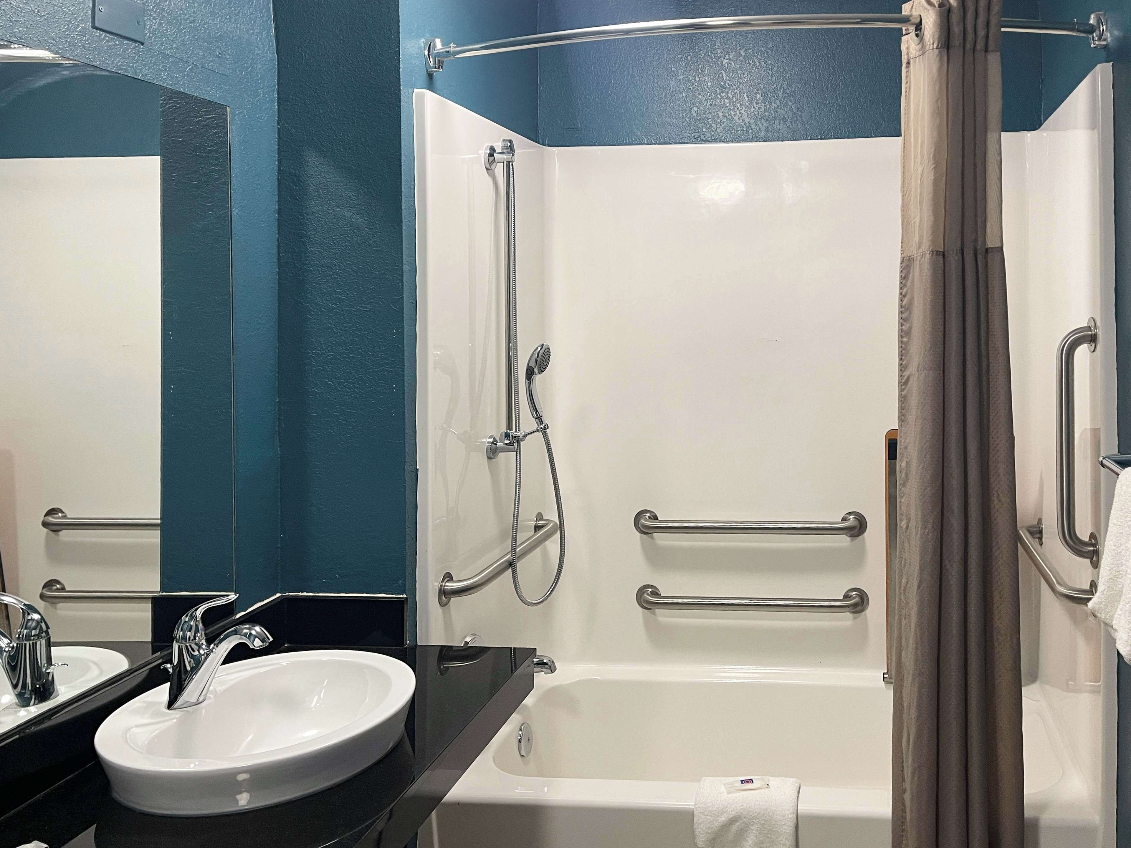 A bathroom with a white bathtub, a sink, and a shower with grab bars.