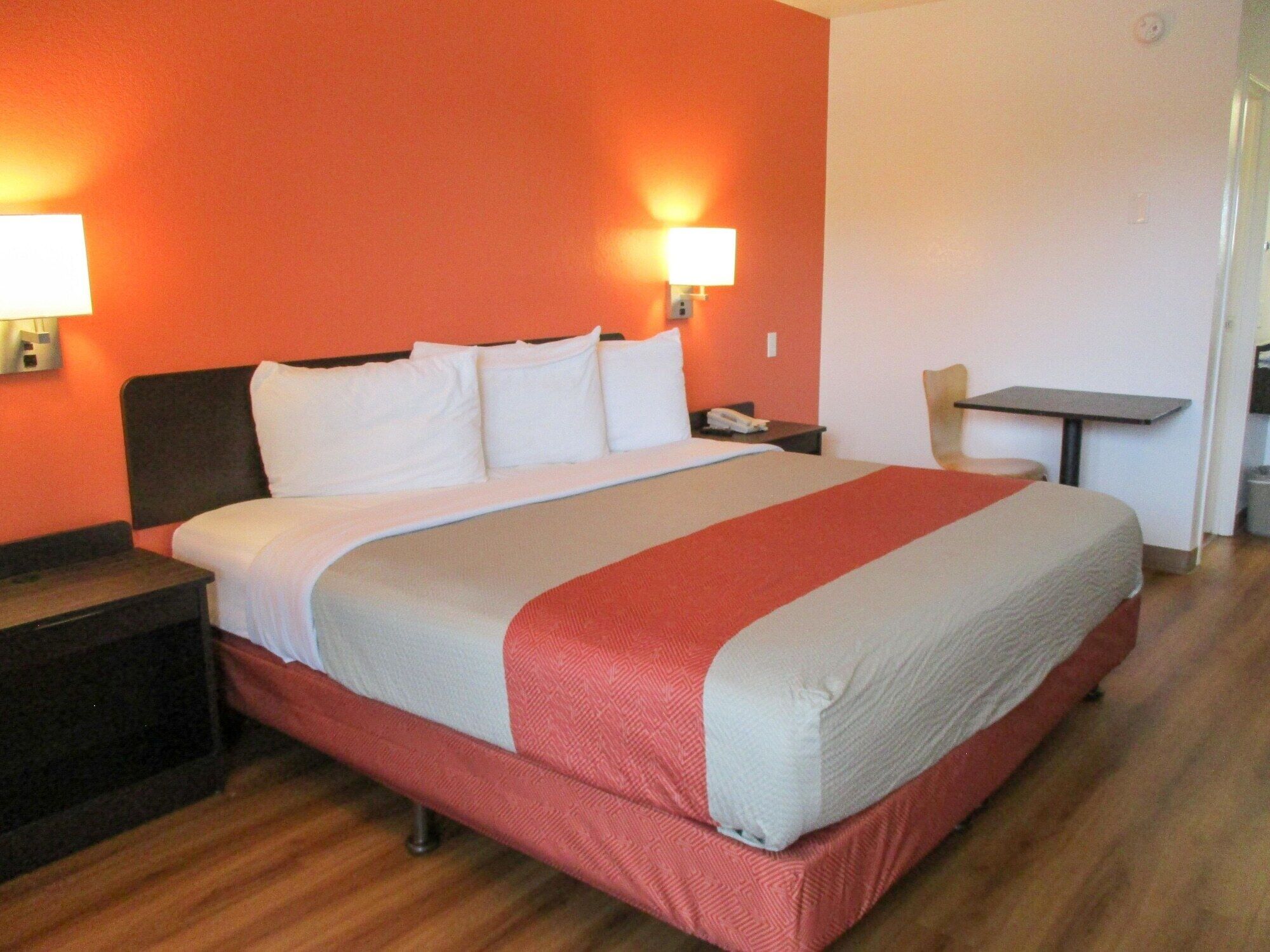 A hotel room with a large bed, a nightstand, a table, and a chair.