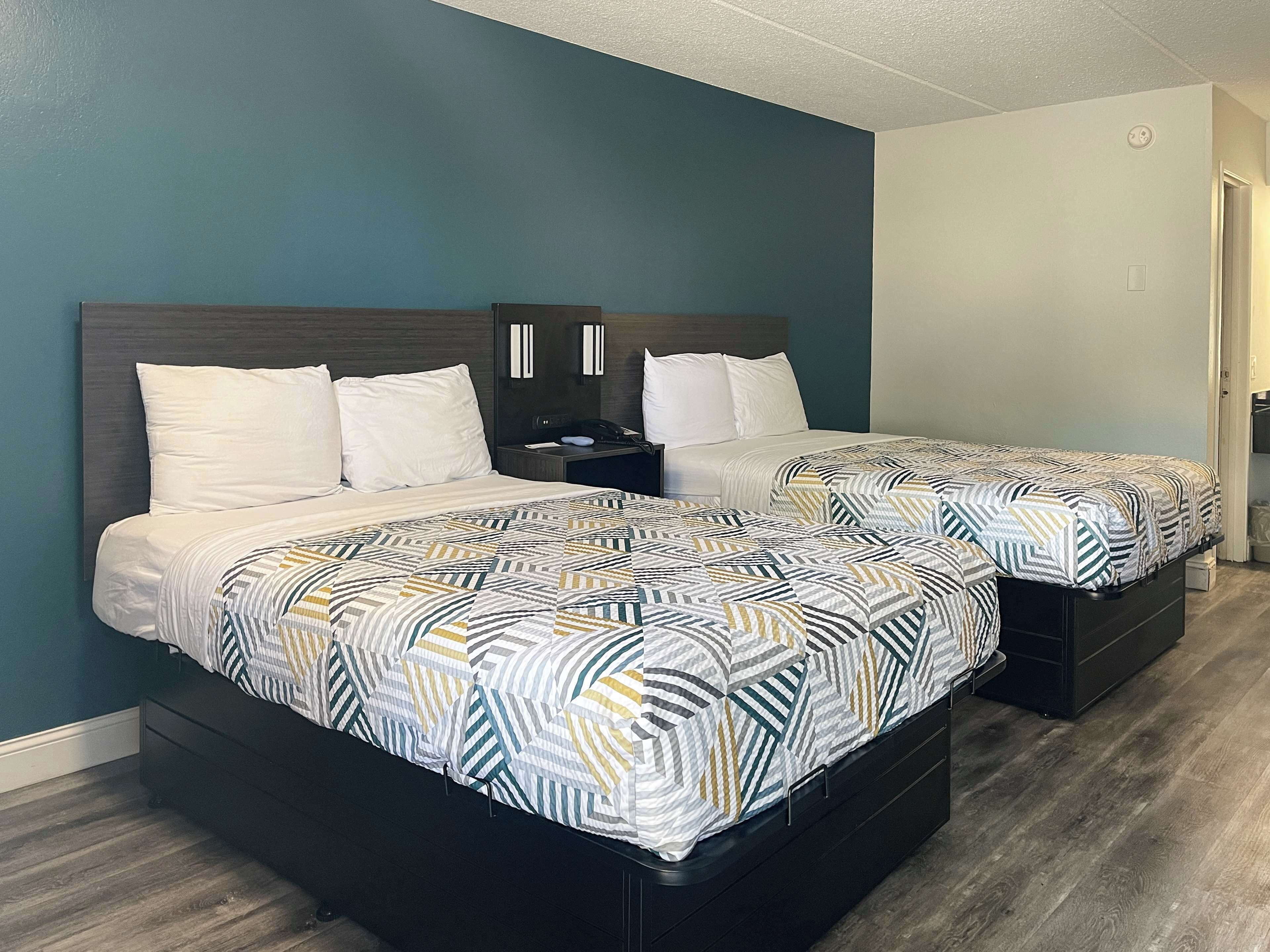 A hotel room with two beds, each with a patterned bedspread, a dark headboard, and a nightstand with a lamp.