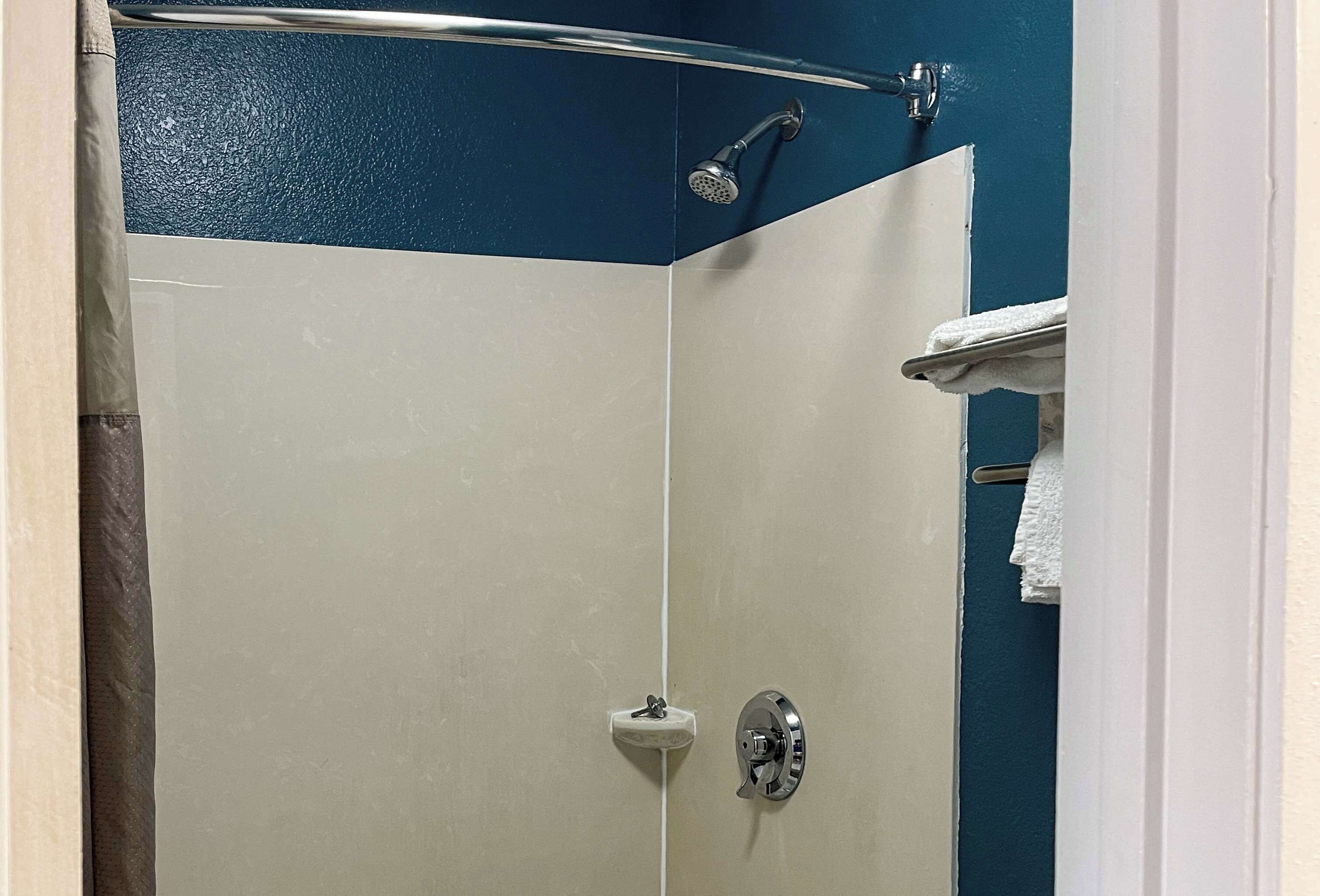 A bathroom with a shower, a towel rack, and a white door.