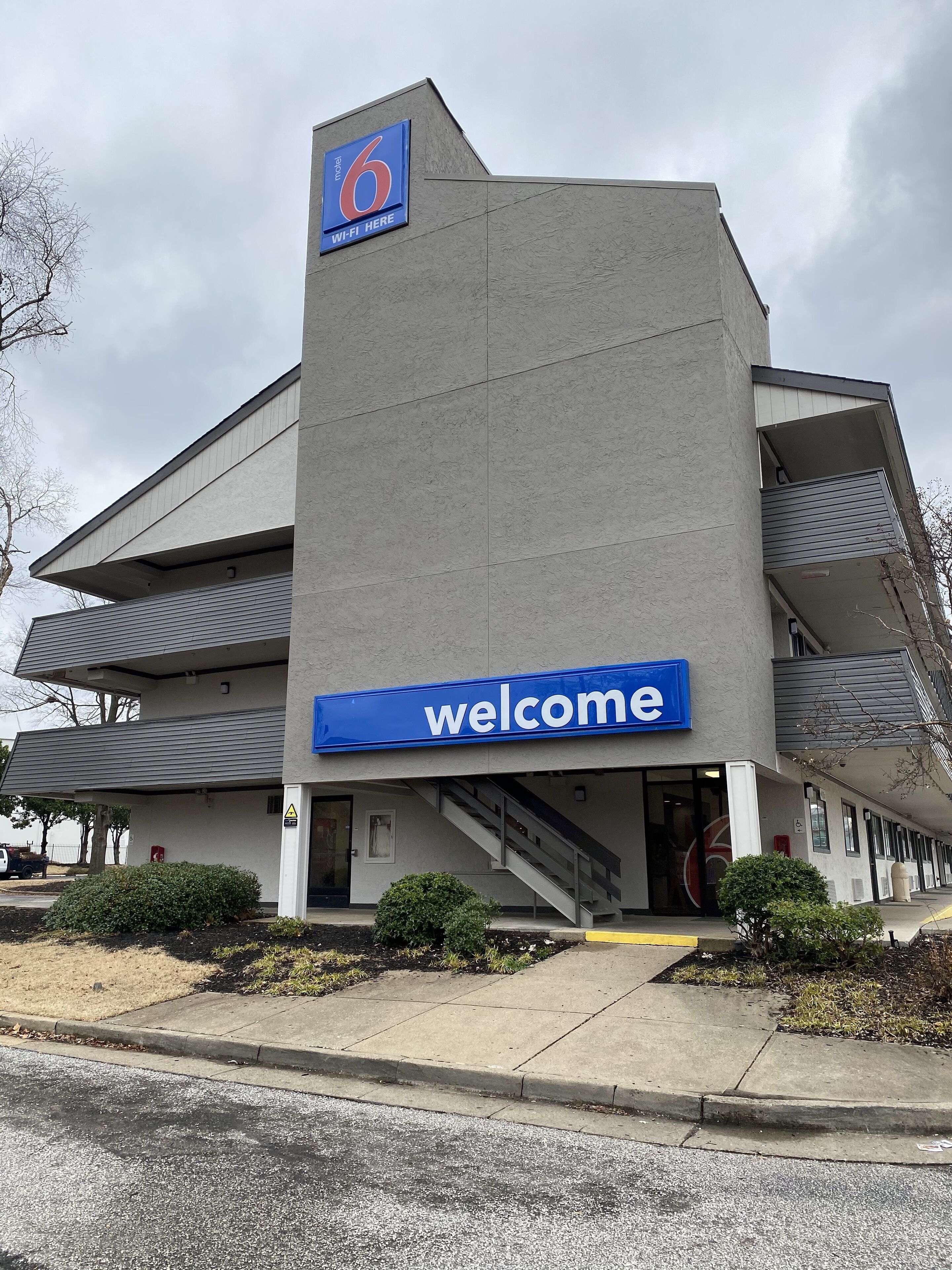 A modern building with a '6' sign indicating a motel, a 'welcome' sign, and a staircase leading to an entrance.