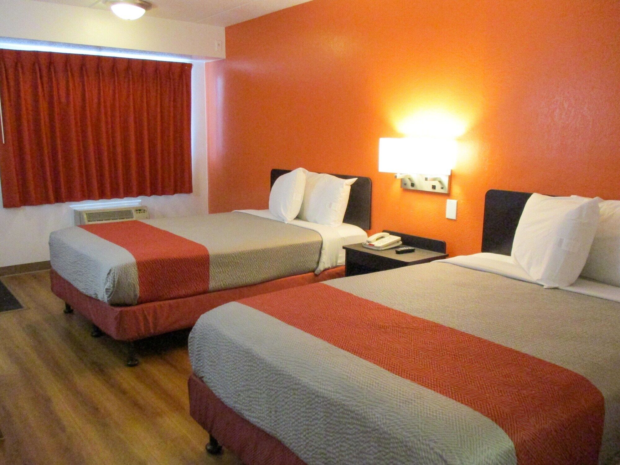 Quarto de hotel com duas camas, mesa de cabeceira, telefone e luminária na parede.