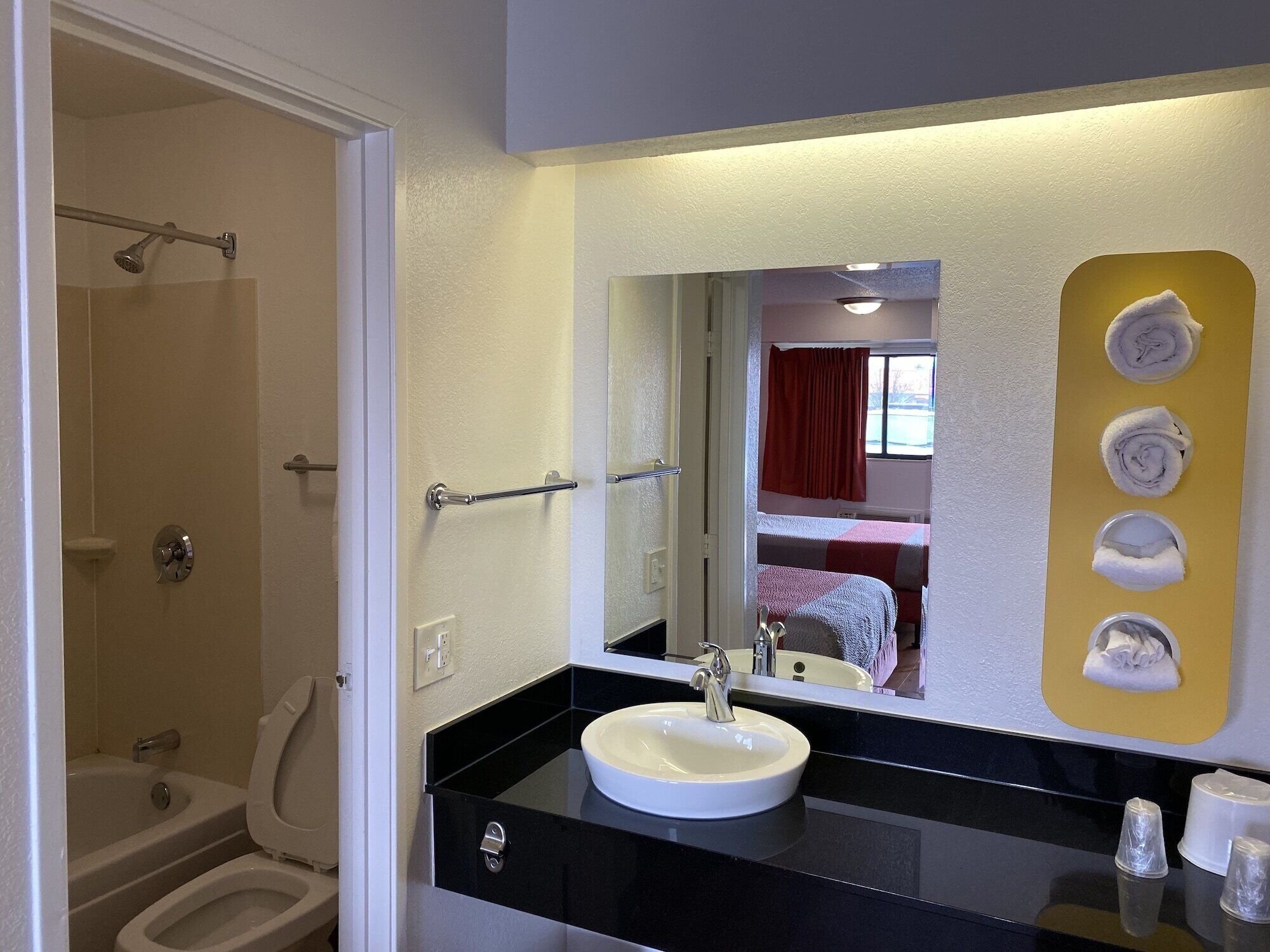 A bathroom with a shower, toilet, sink, and a mirror with a yellow towel rack.