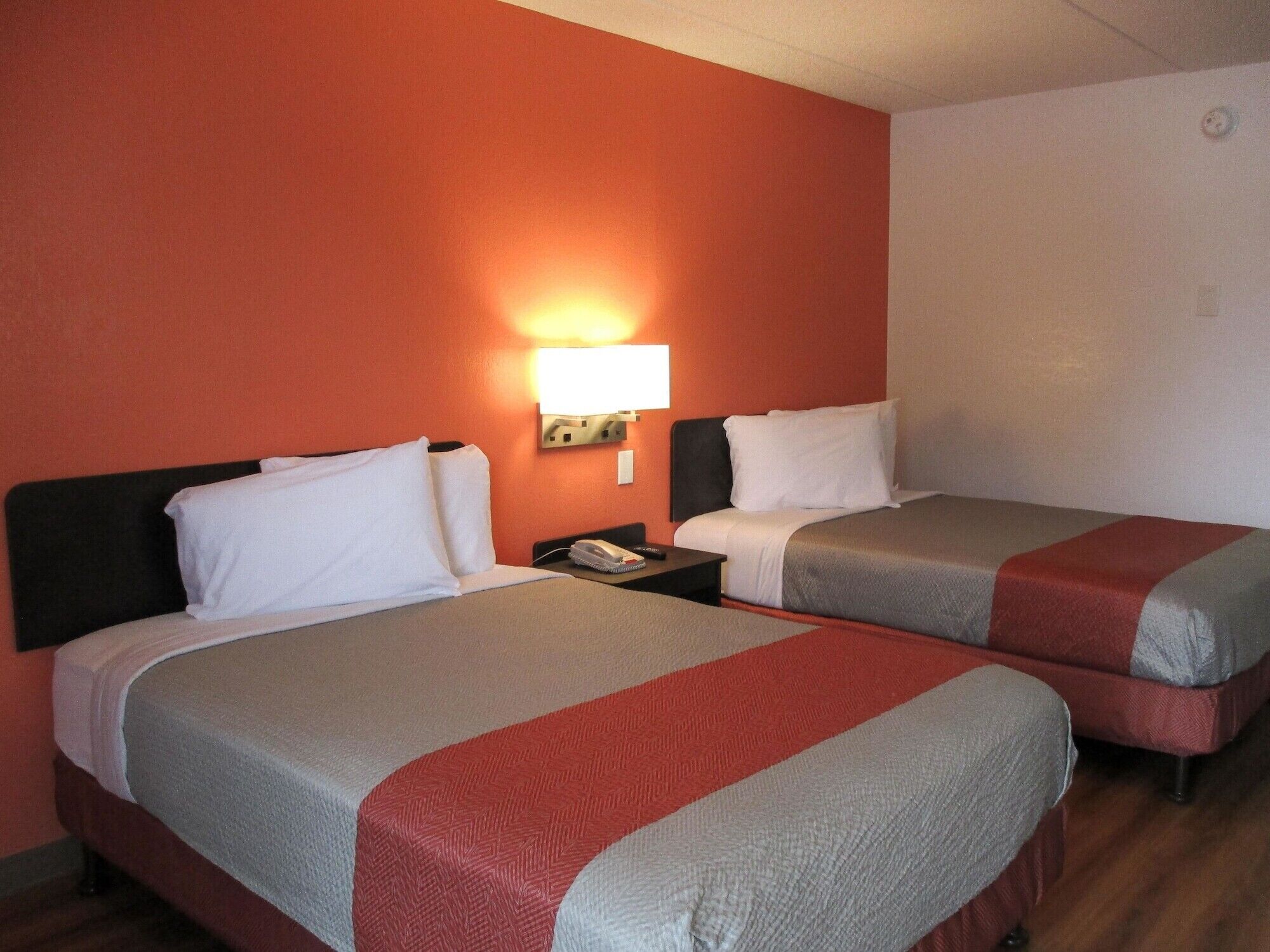 A hotel room with two beds, each with a headboard, a nightstand, and a wall-mounted lamp.
