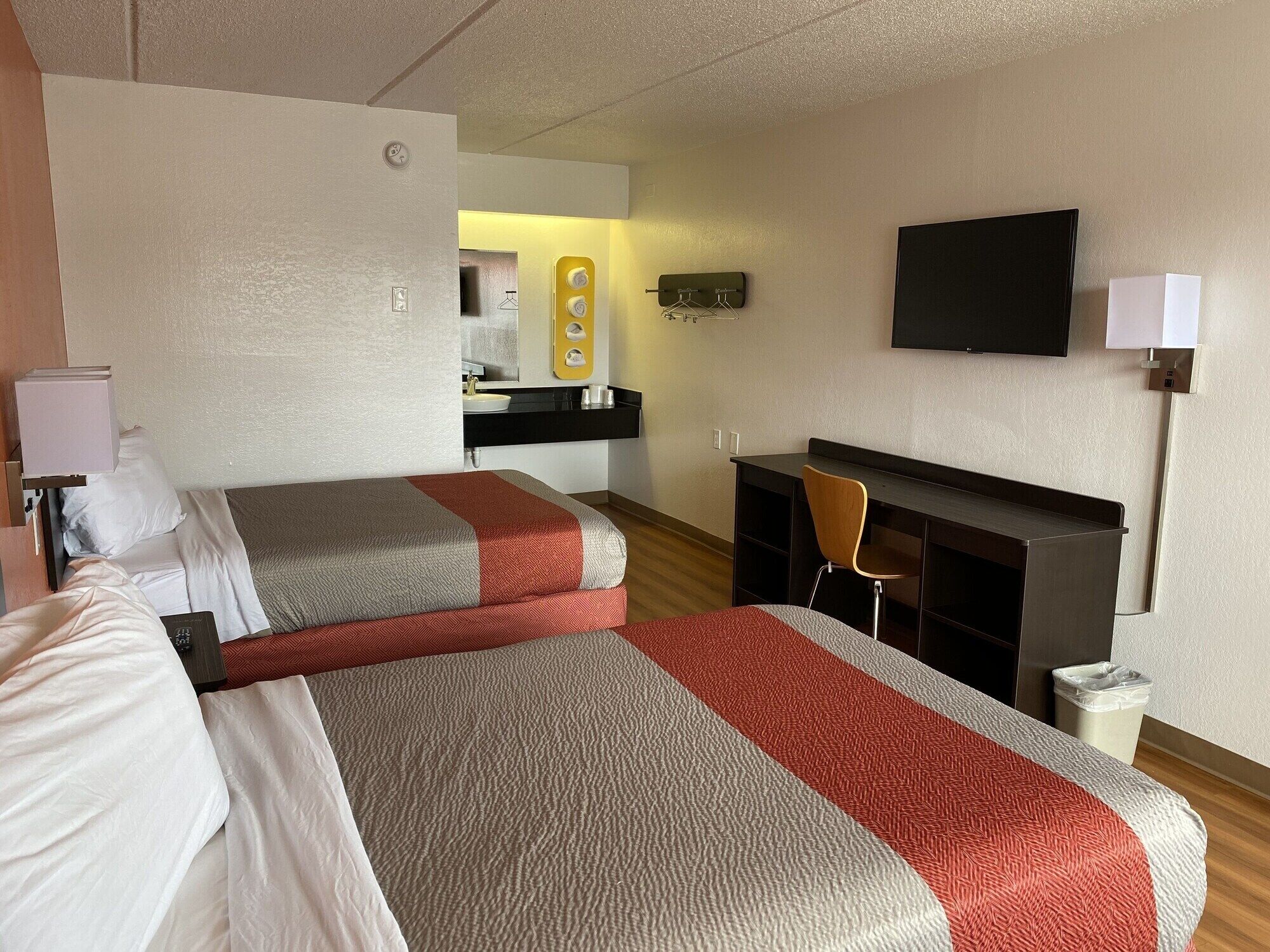 Une chambre d’hôtel avec deux lits, un bureau, une chaise, une télévision et une poubelle.