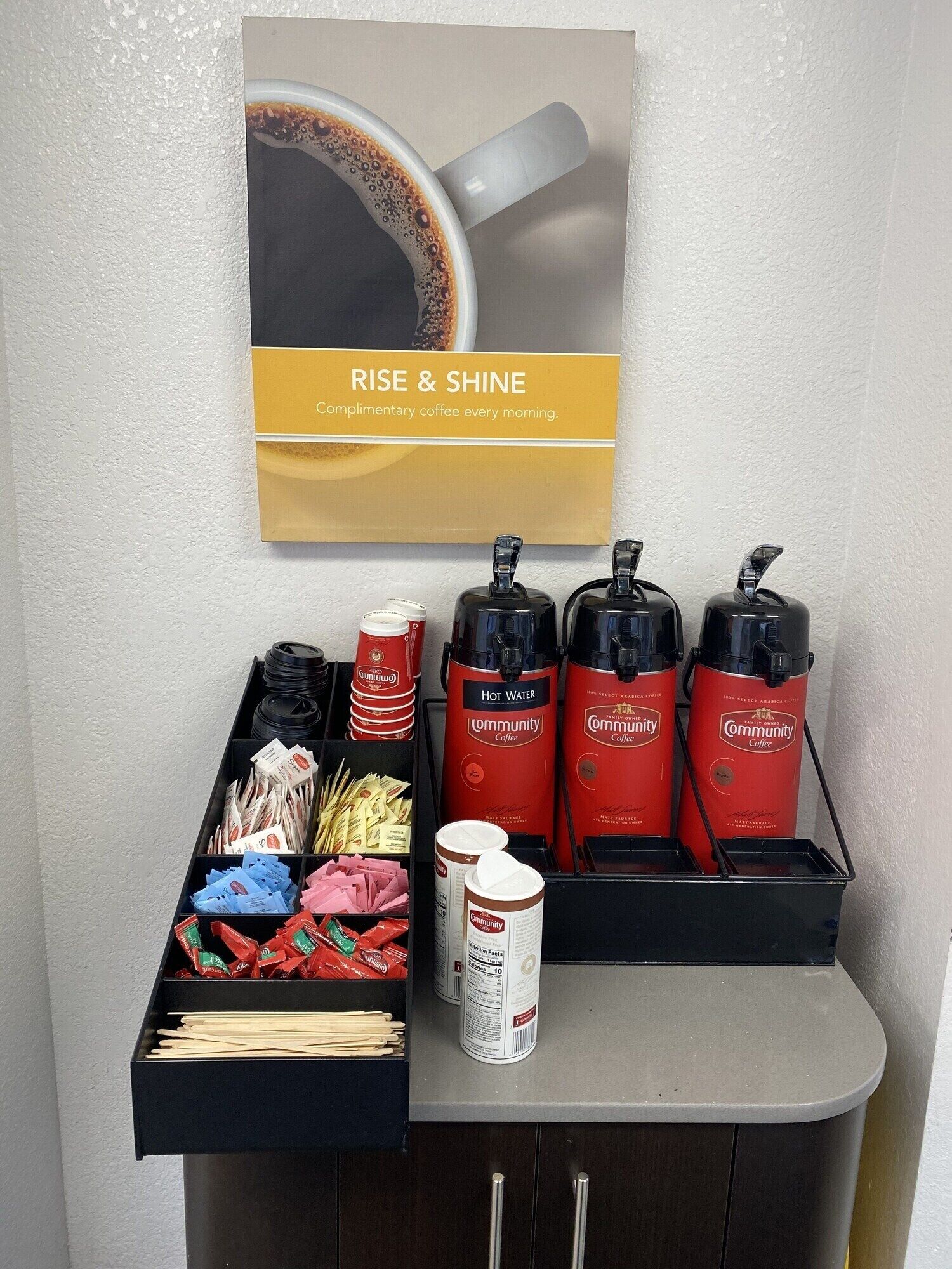 A coffee station with a sign that reads "RISE & SHINE Complimentary coffee every morning."