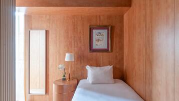 A hotel room with a wooden wall, a bed with white bedding, a round bedside table with a lamp, and a framed picture on the wall.