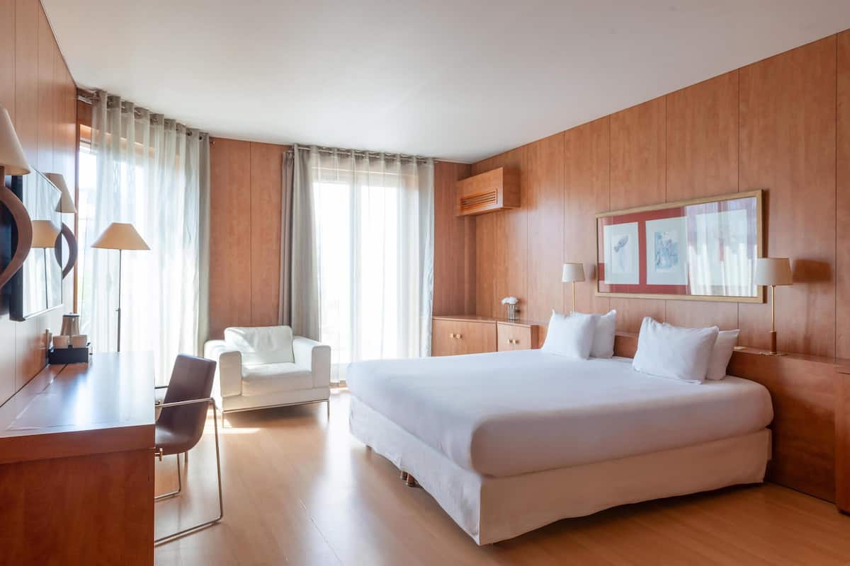 A hotel room with a large bed, a desk with a chair, a small sofa, and a wall-mounted TV.
