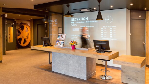 Un mostrador de recepción con una pantalla digital que muestra información, una gran rueda de madera y un diseño de interiores moderno.