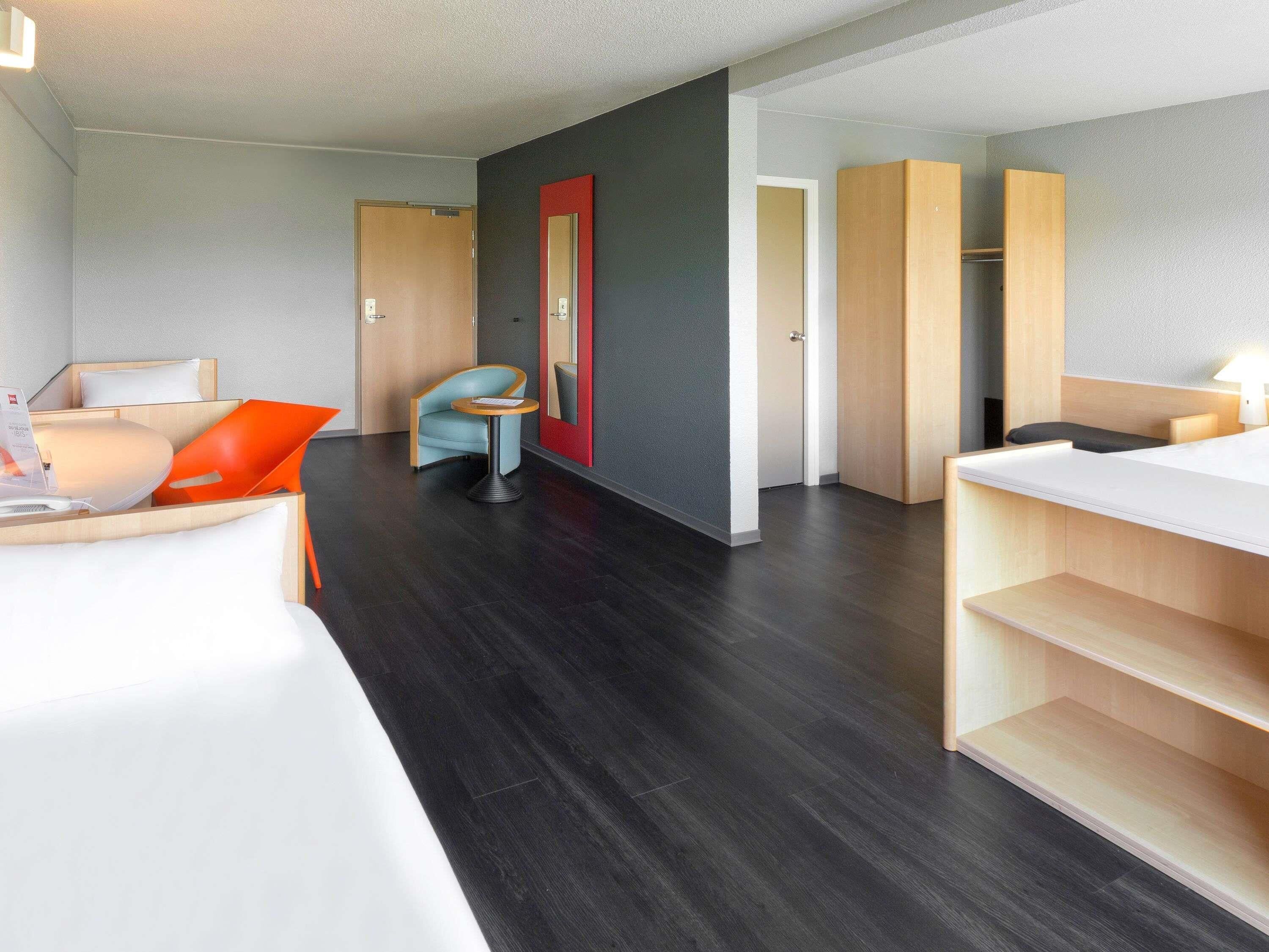A modern hotel room with a bed, a small table, a chair, and a desk.