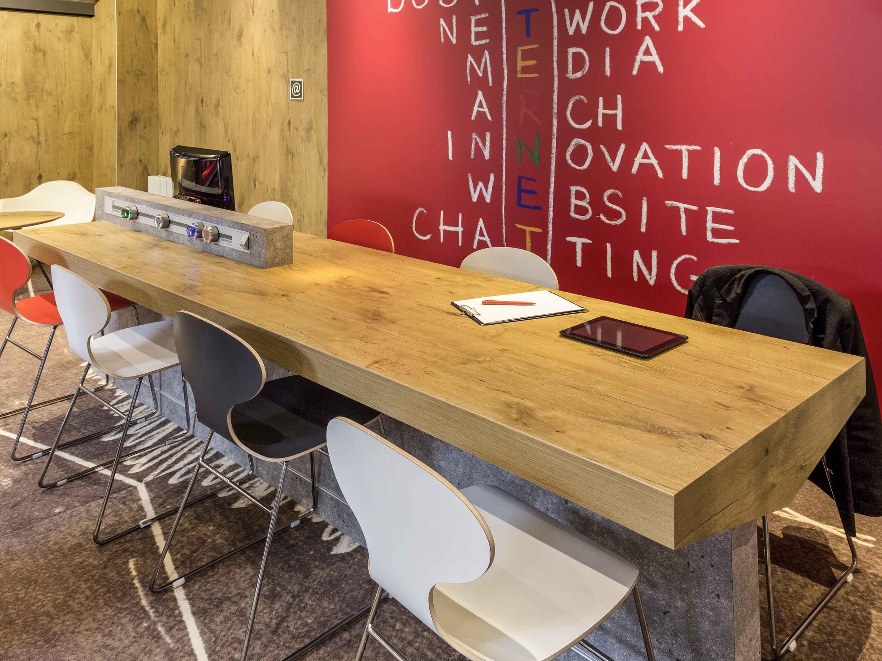A conference room with a long wooden table, white chairs, a projector, and a red wall with white text.