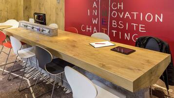 A conference room with a long wooden table, white chairs, a projector, and a red wall with white text.