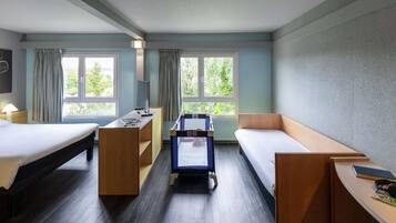 A hotel room with two beds, a desk, a chair, a small table, and a window with a view of greenery.