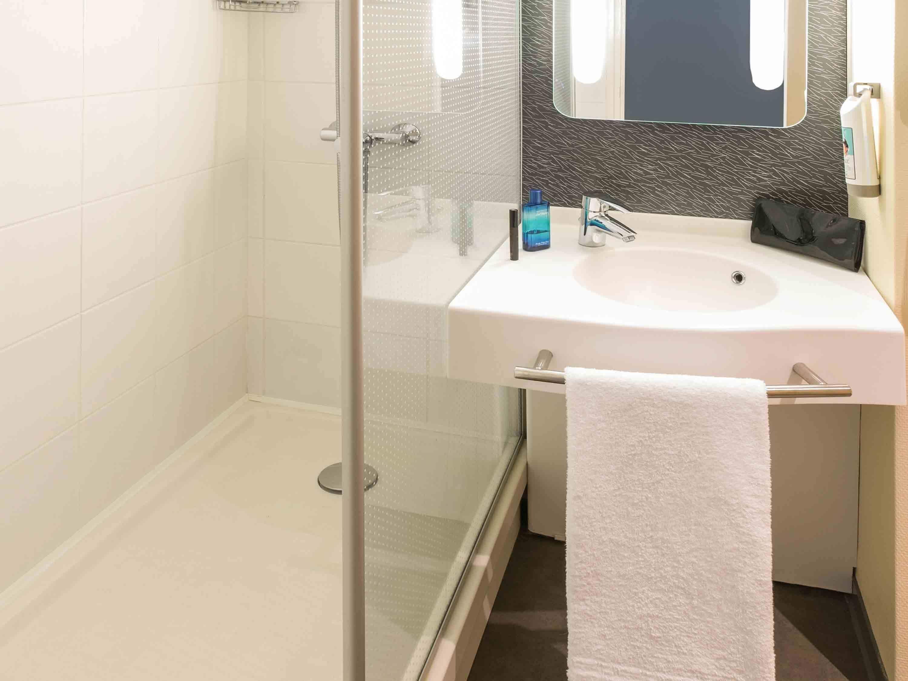 Un baño con cabina de ducha de vidrio, un lavamanos blanco, un espejo y un perchero para toallas.