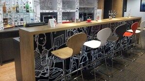 Zona de bar con mostrador, taburetes y una variedad de botellas y vasos.