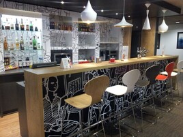 Zona de bar con mostrador, taburetes y una variedad de botellas y vasos.