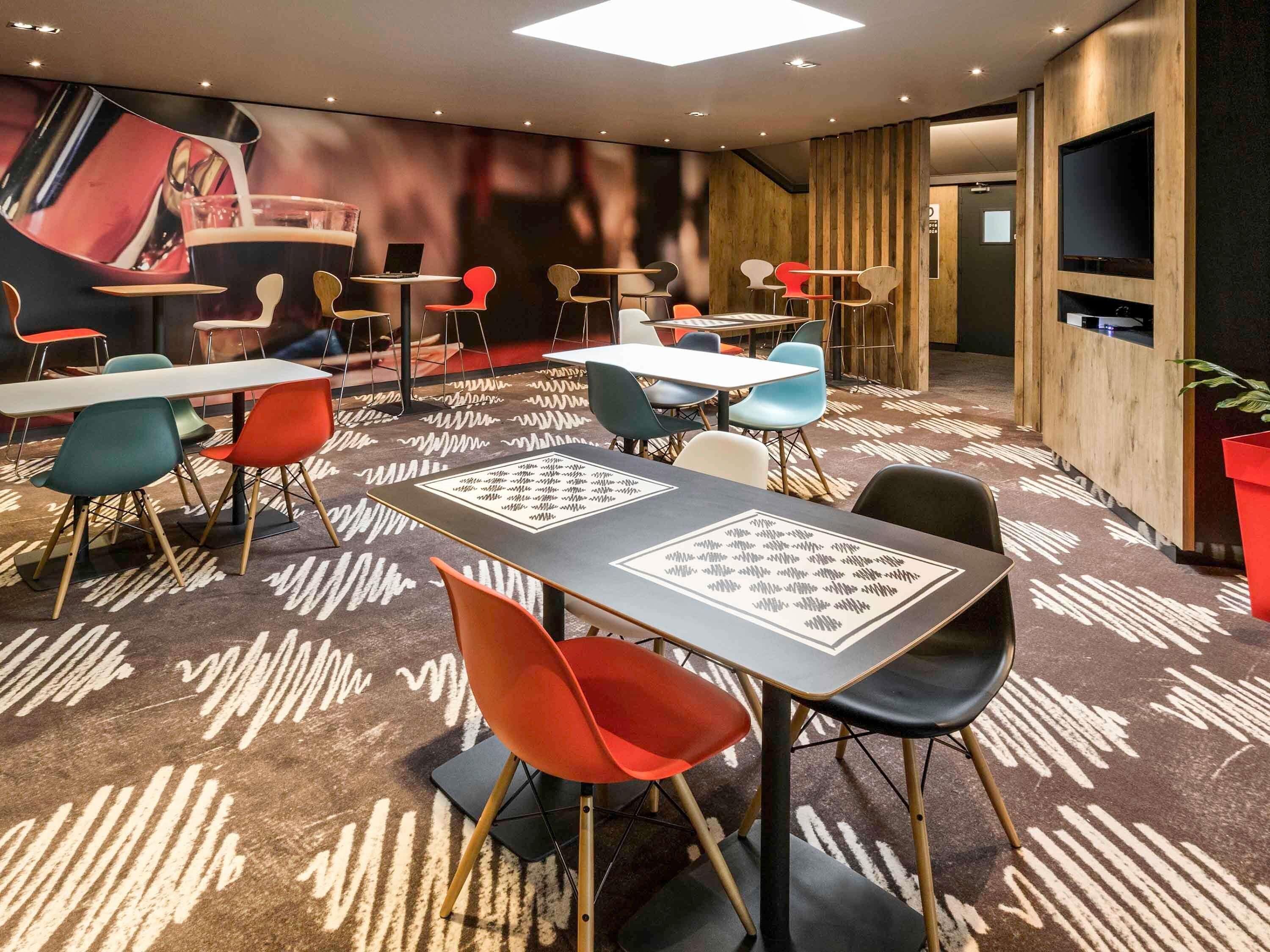 A modern hotel room with a large bed, a flat-screen TV, and a seating area with tables and chairs.