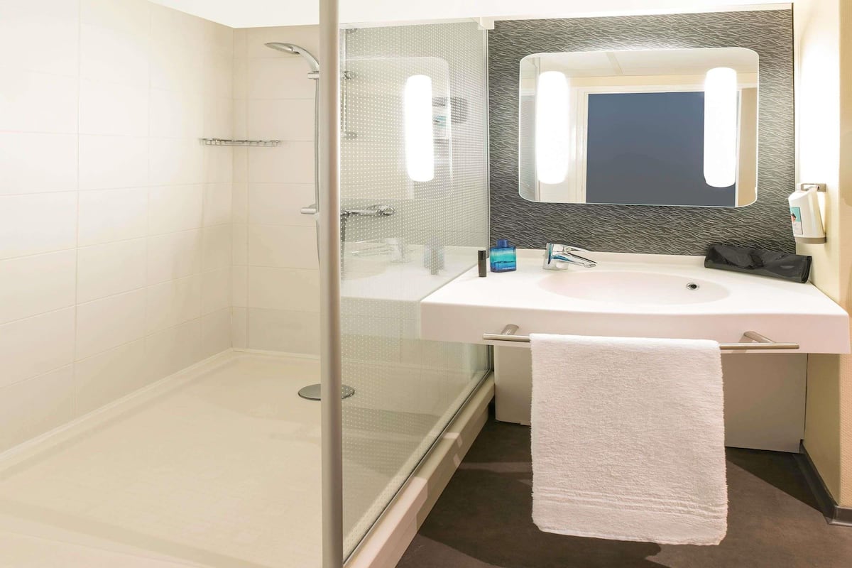 A modern bathroom with a glass-enclosed shower, a white sink, and a large mirror.