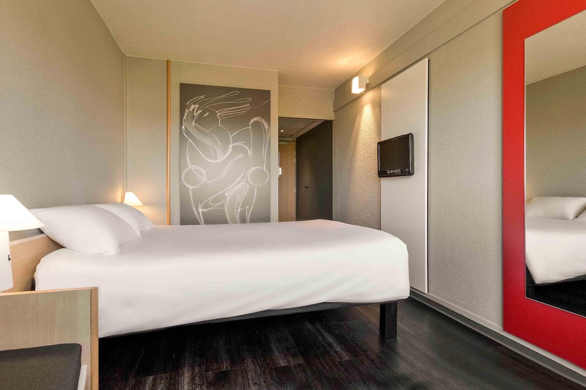 A hotel room with a bed, bedside lamps, a TV, and a large mirror.