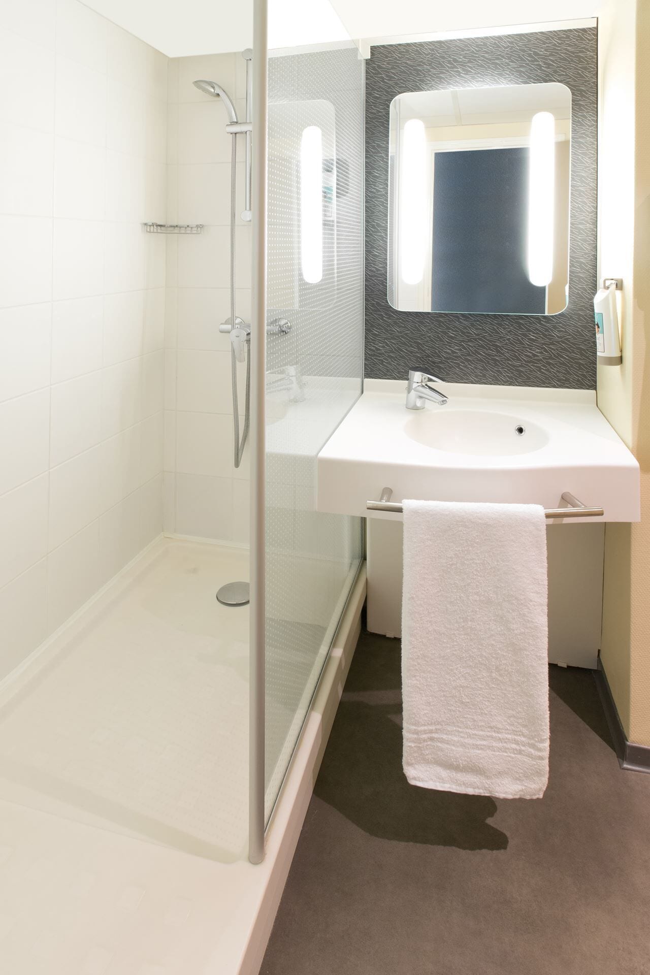 A modern bathroom with a glass-enclosed shower, a white sink, and a large mirror above the vanity.