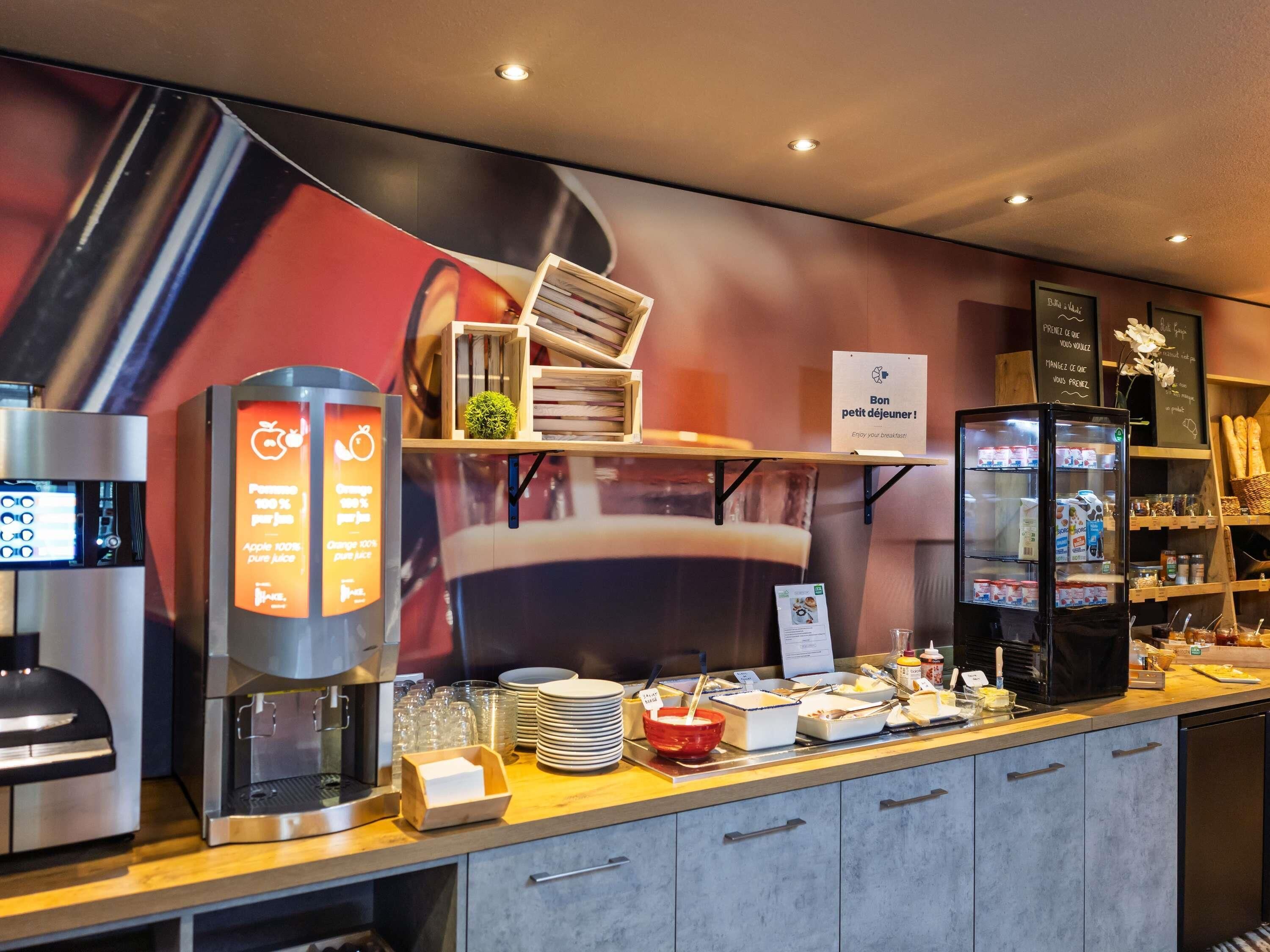 A breakfast bar with a coffee machine, a fruit juicer, and a refrigerator stocked with beverages.