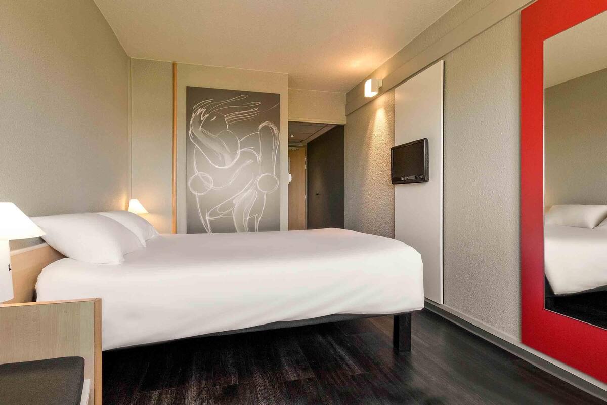 Ein Hotelzimmer mit Bett, Nachttischlampen, einem Fernseher und einem großen Spiegel.