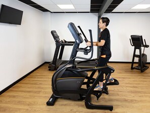 Een sportschool met loopbanden, een hometrainer en een roeimachine.