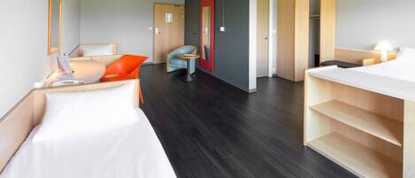 Una habitación de hotel con una cama, un escritorio, una silla, un espejo y un armario.