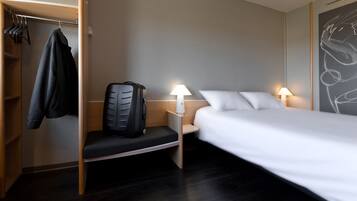 Ein Hotelzimmer mit einem Bett, zwei Nachttischlampen, einem Schreibtisch mit Stuhl, einem Kleiderständer und einem Koffer.