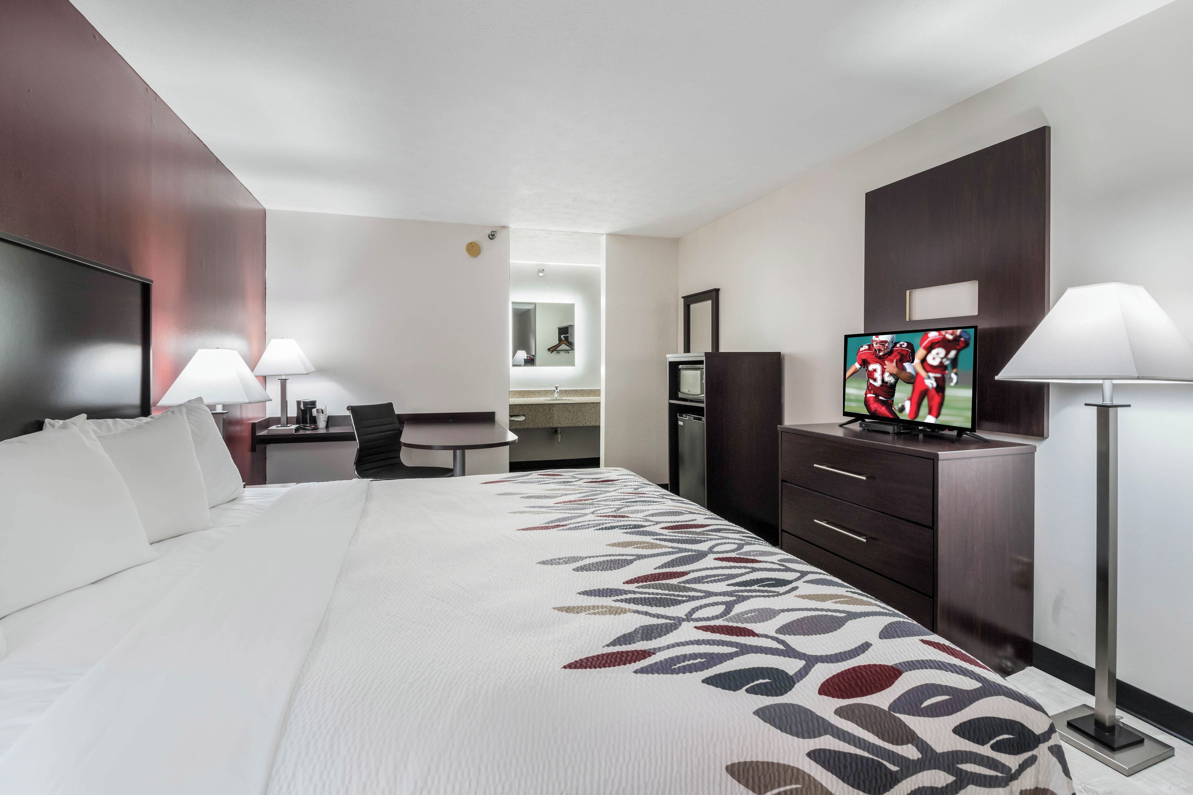 A hotel room with a large bed, a desk, a TV, and a dresser.