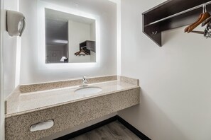 A bathroom with a granite countertop sink, a mirror, a towel rack, and a wall-mounted towel dispenser. - Red Roof Inn Cadiz (Cadiz)