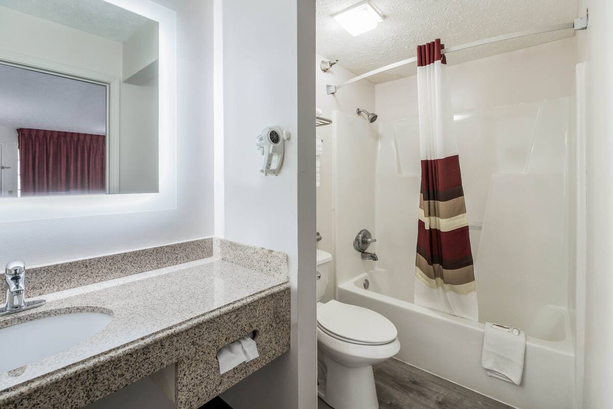 A bathroom with a granite countertop sink, a toilet, and a bathtub with a shower curtain.
