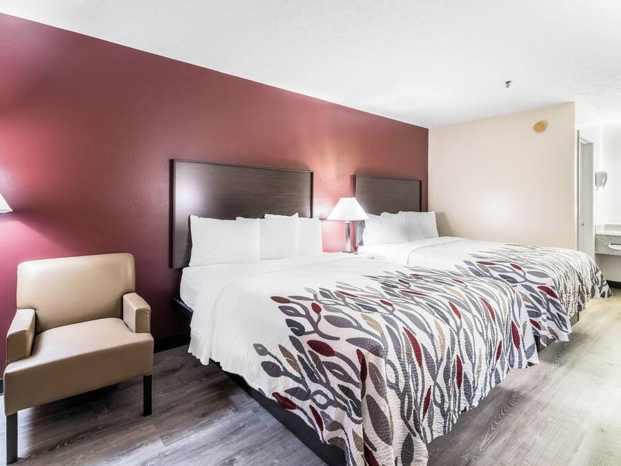 A hotel room with a bed, a chair, a nightstand, and a lamp.