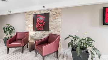 A Red Roof Inn reception area with two leather chairs, a stone wall, and potted plants.
