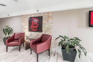 A Red Roof Inn reception area with two leather chairs, a stone wall, and potted plants. - Red Roof Inn Cadiz (Cadiz)