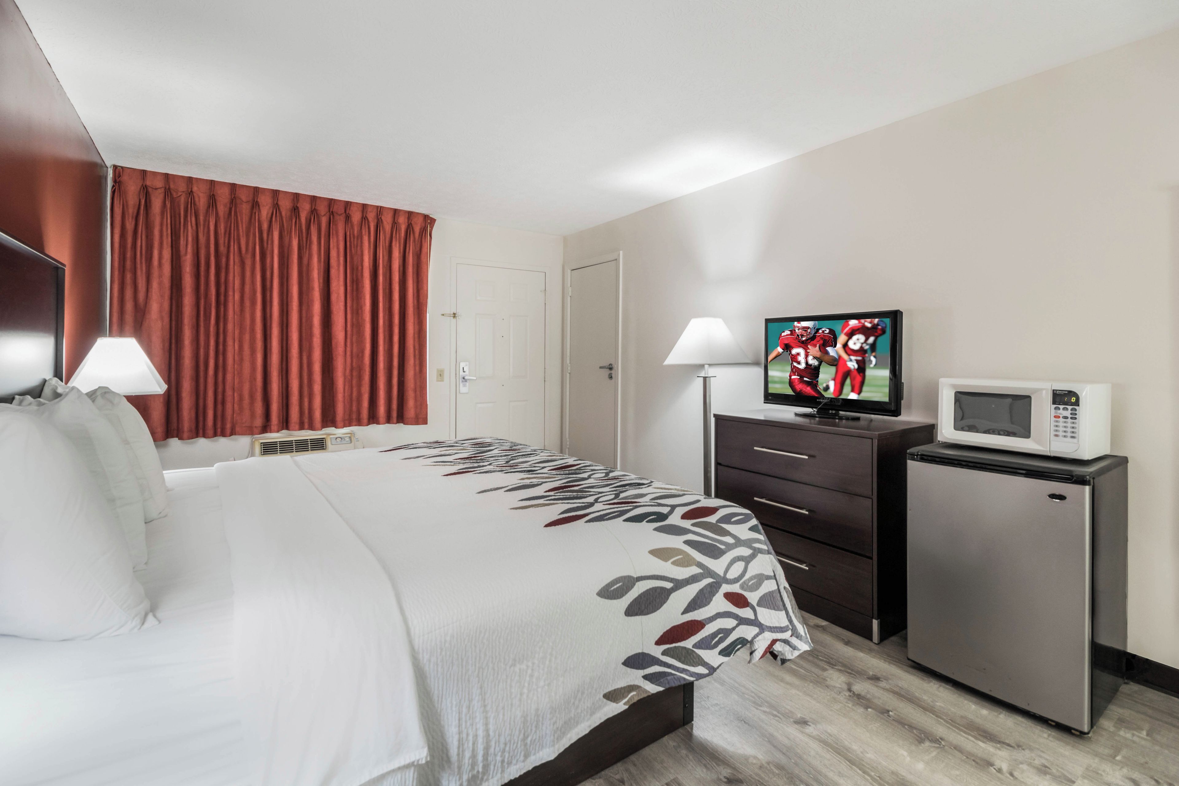 A hotel room with a bed, a television, a microwave, and a small refrigerator.