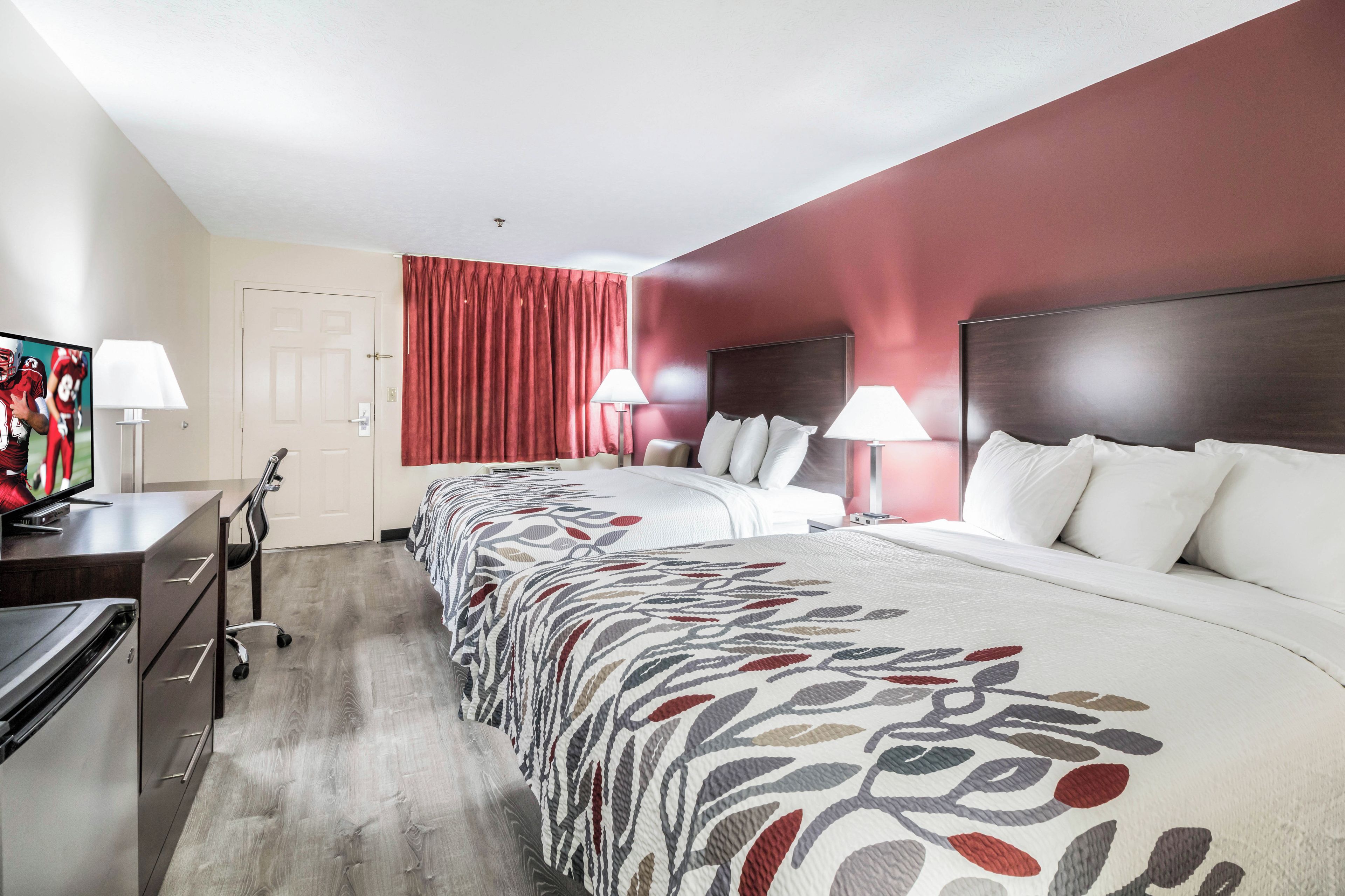 A hotel room with a large bed, two bedside tables with lamps, a TV on a desk, and a door with a curtain.