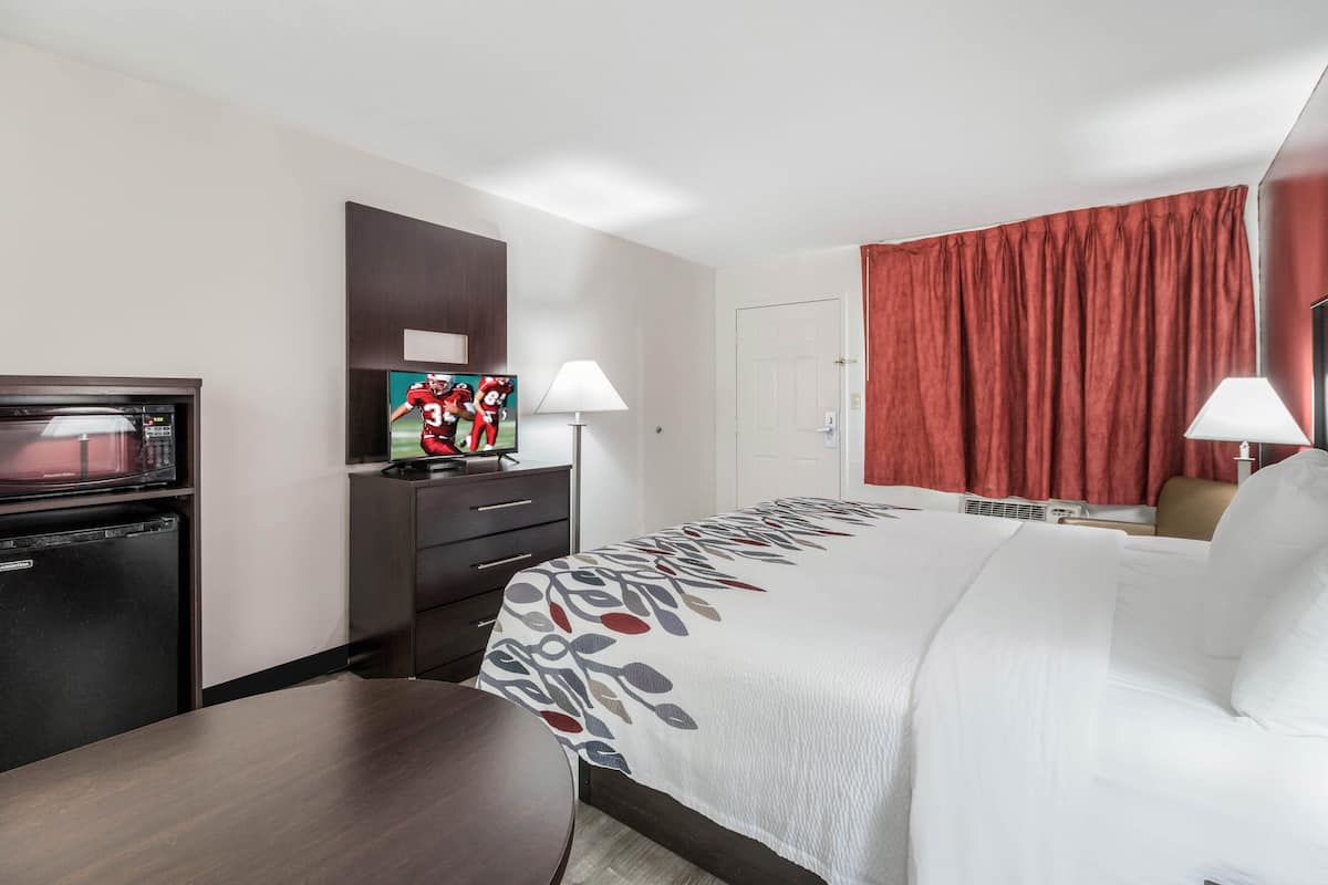 Ein Hotelzimmer mit Bett, Schreibtisch, Mikrowelle, Fernseher und einem roten Vorhang.