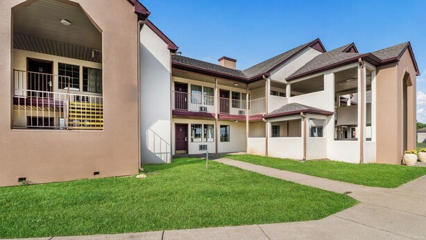 A multi-story residential building with a covered patio area and a well-maintained lawn. - Red Roof Inn Cadiz (Cadiz)
