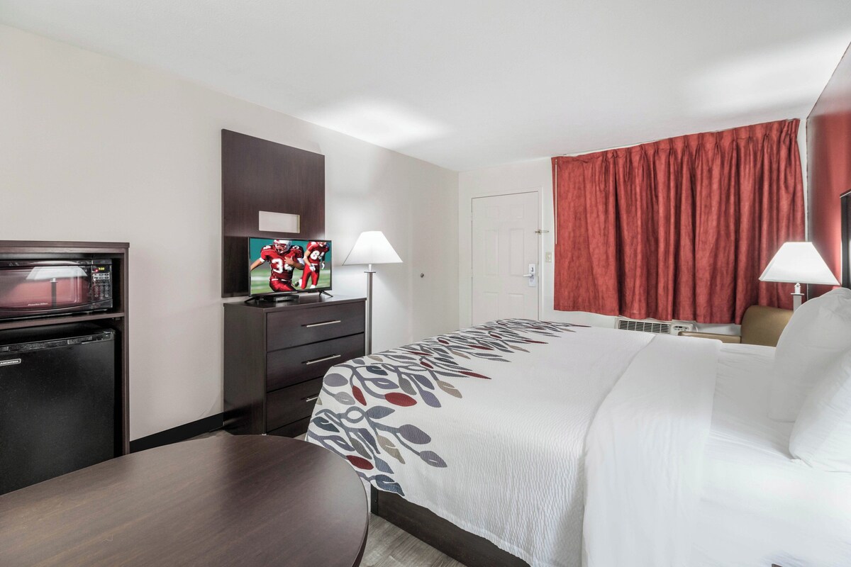 A hotel room with a bed, a desk, a microwave, a television, and a lamp.