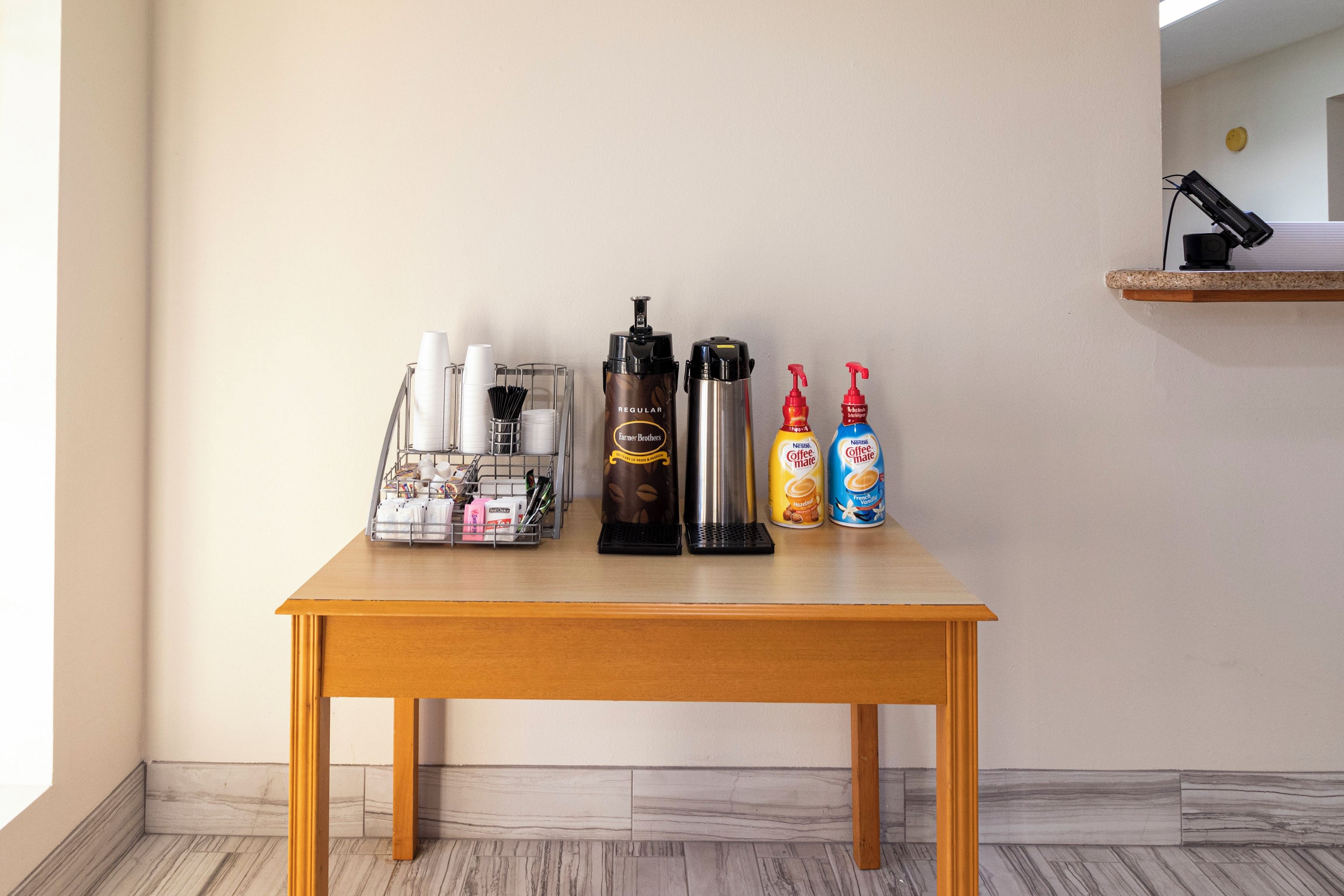 Een houten tafel met een koffieapparaat, een thermoskan en twee flessen koffiemelk.