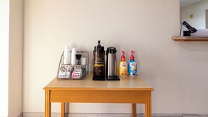 A wooden table with a coffee machine, a thermos, and two bottles of coffee creamer. - Red Roof Inn Cadiz (Cadiz)
