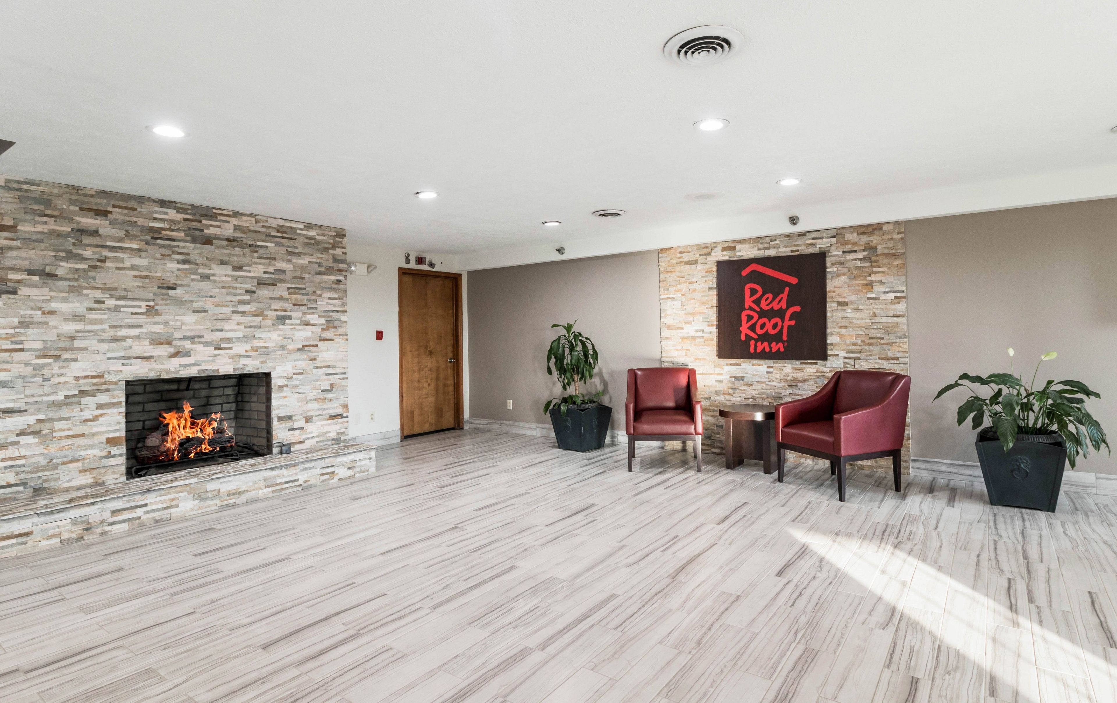 Un vestíbulo de hotel con una pared de piedra, una chimenea, dos sillones de cuero y un letrero de Red Roof Inn.