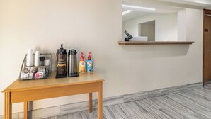 A hotel room with a wooden table, a coffee machine, and a shelf with coffee and cream dispensers. - Red Roof Inn Cadiz (Cadiz)