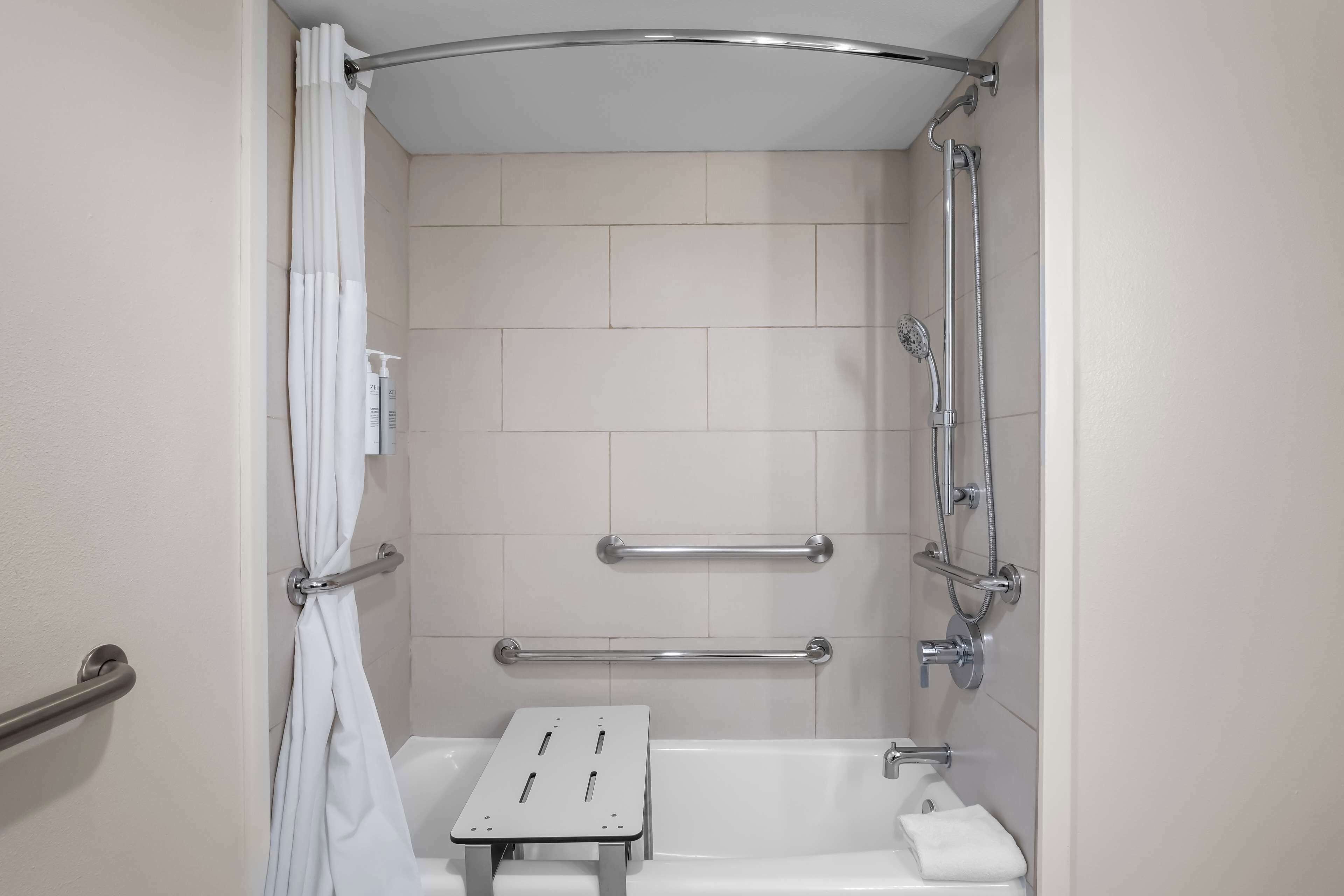 A shower with a grab bar, a white towel, and a handheld showerhead.