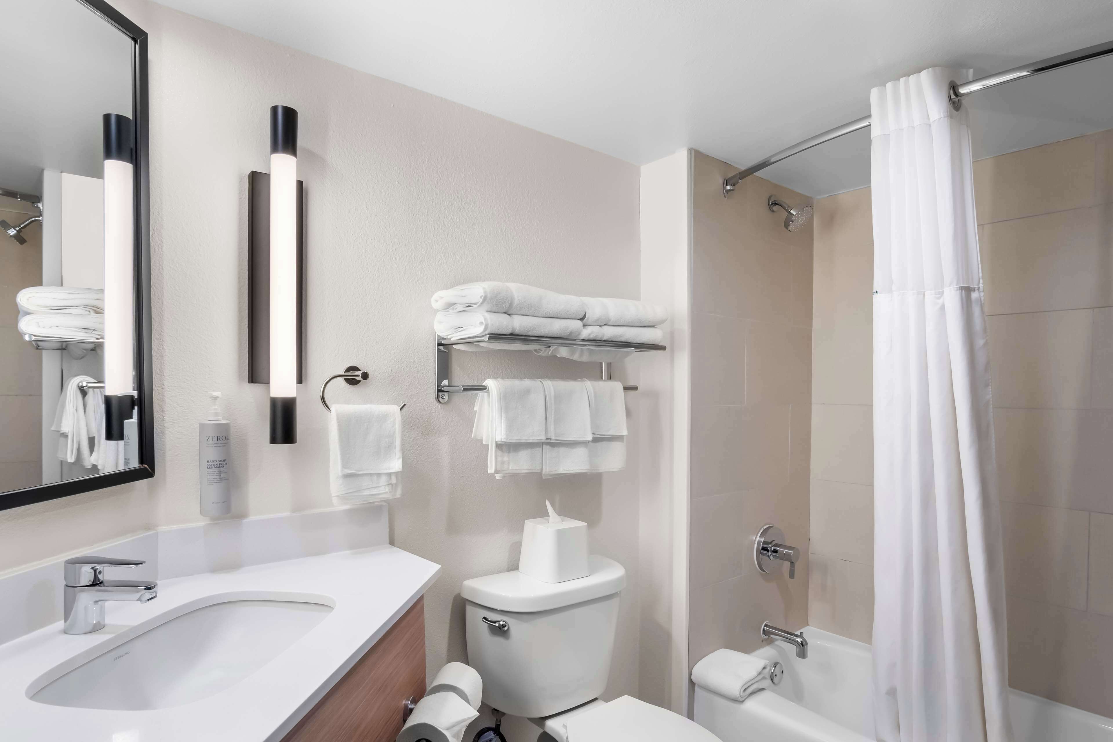 A modern bathroom with a sink, toilet, and shower. There are towels and toiletries visible.