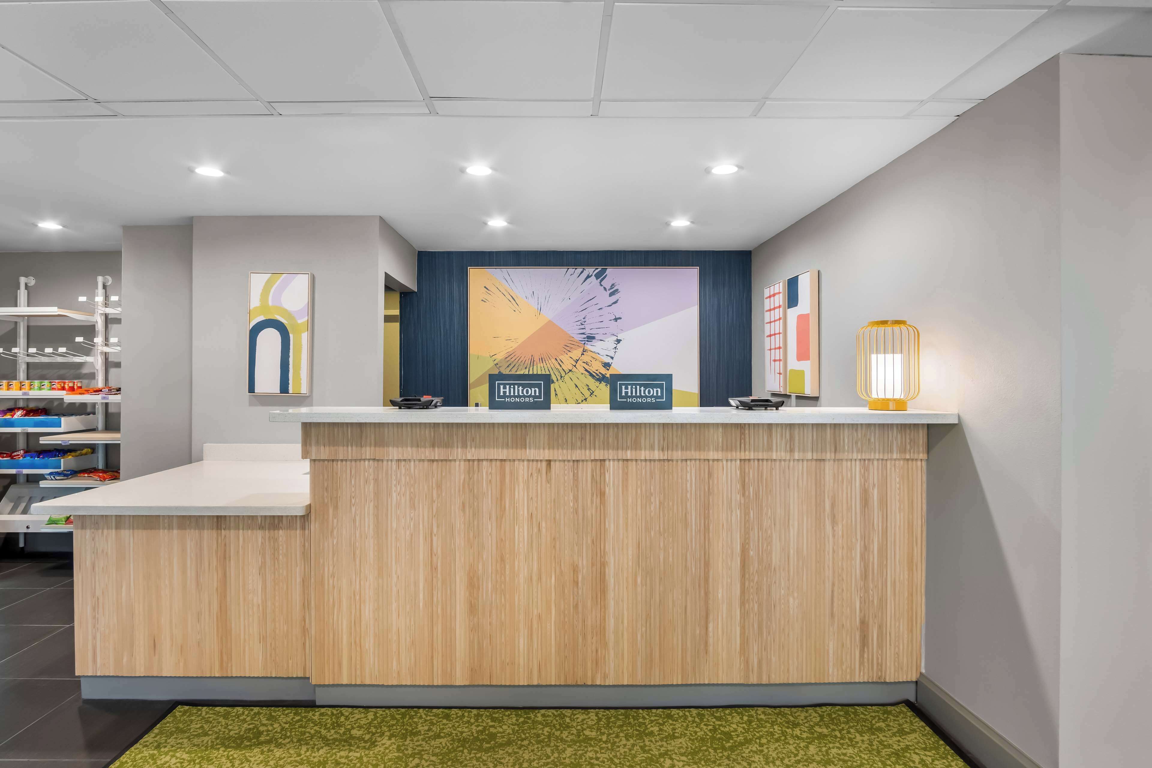 A reception desk with a wooden finish, a large abstract painting on the wall, and a sign indicating 'Hilton Honors' on the counter.